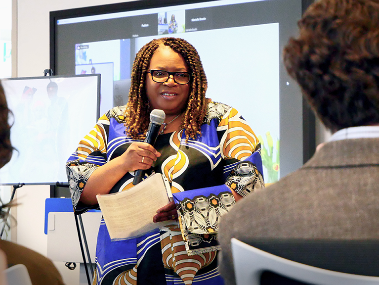 A person dressed in traditional multicoloured clothes speaks into a microphone.